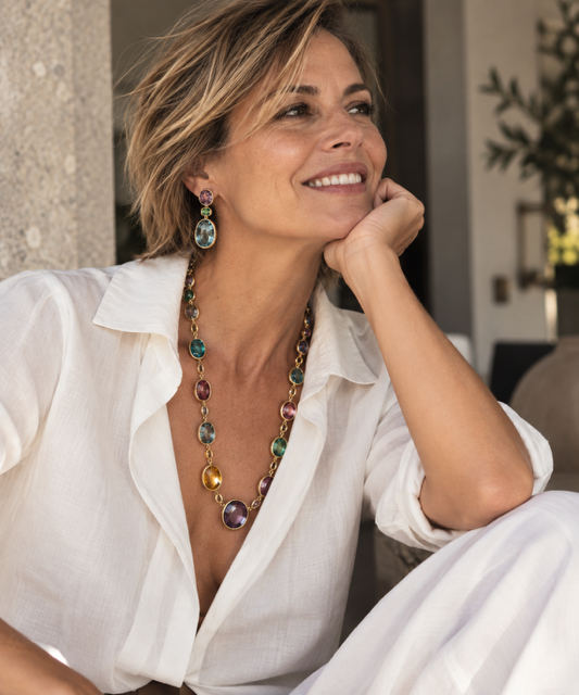 Woman smiling in a white linen shirt wearing a colorful gemstone necklace and drop earrings